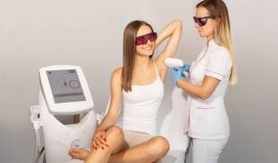 Kosmetolog przeprowadza depilację laserową pach uśmiechniętej brunetce.