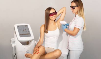 Kosmetolog przeprowadza depilację laserową pach uśmiechniętej brunetce.