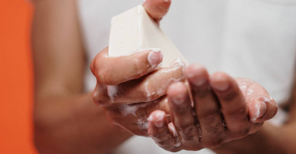 Zbliżenie na namydlone dłonie mężczyzny trzymające białe mydło w kostce.
